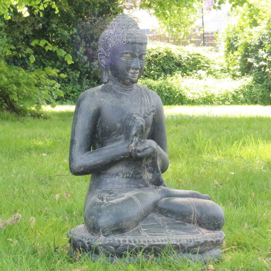 Steinbuddha seitlich im Garten auf einer grünen Wiese