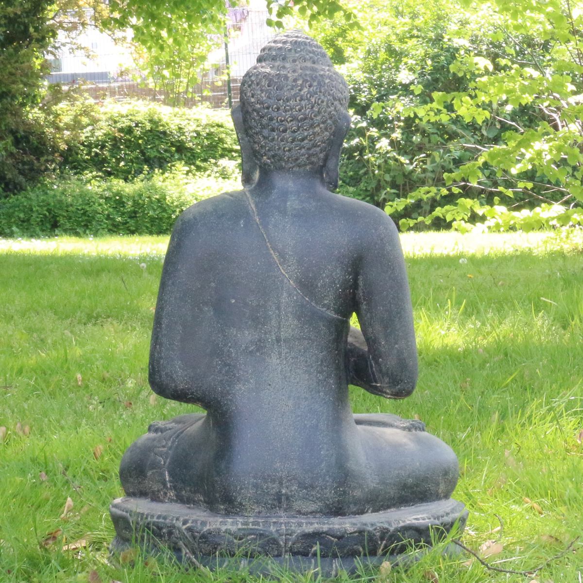 Steinbuddha von hinten im Garten auf einer grünen Wiese