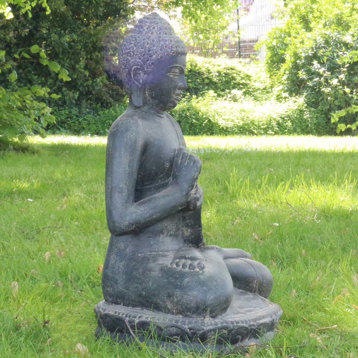 Steinbuddha seitlich im Garten auf einer grünen Wiese